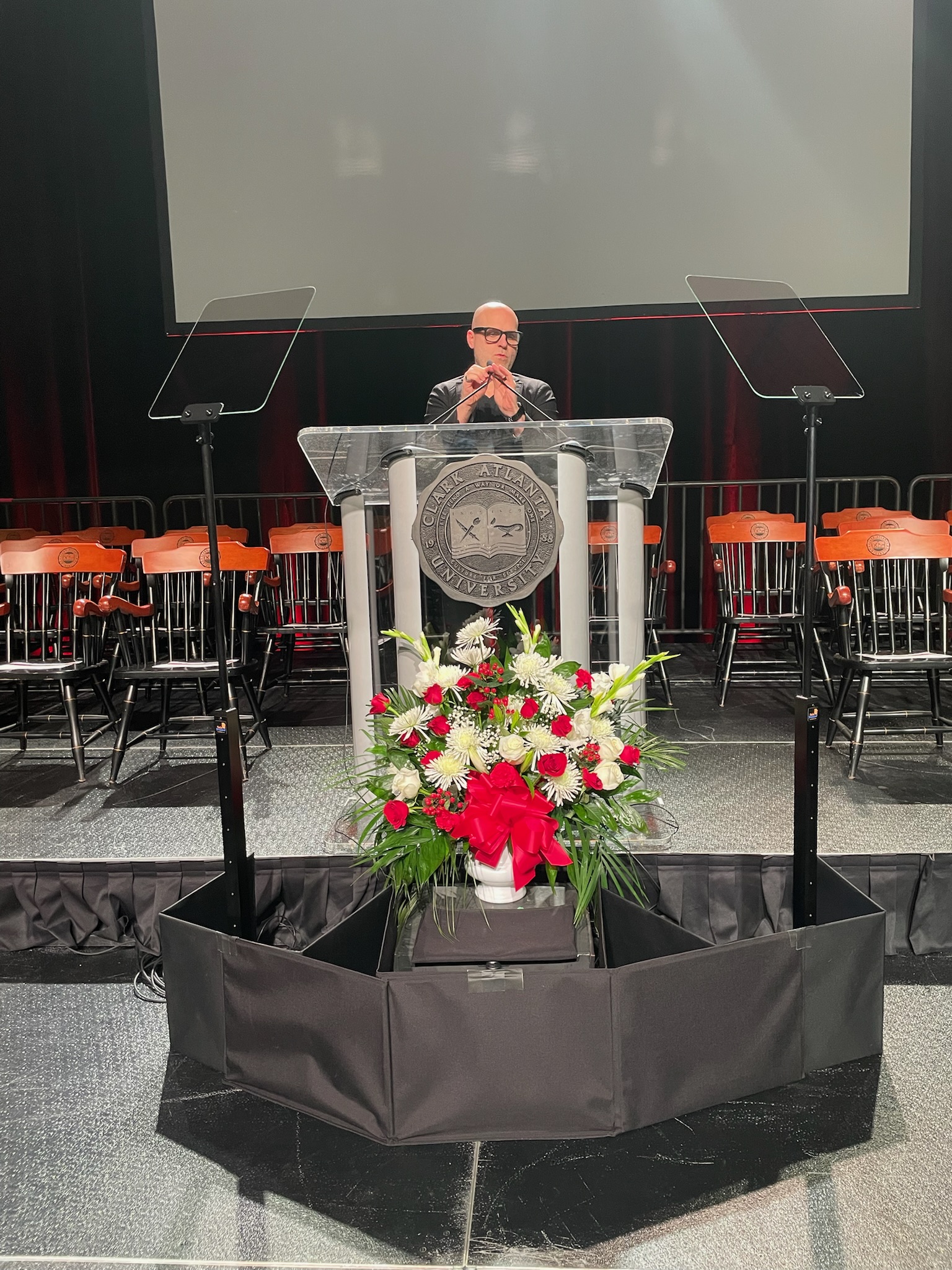Speaker at a clear acrylic podium with dual teleprompter glass panels at a Clark Atlanta University ceremony