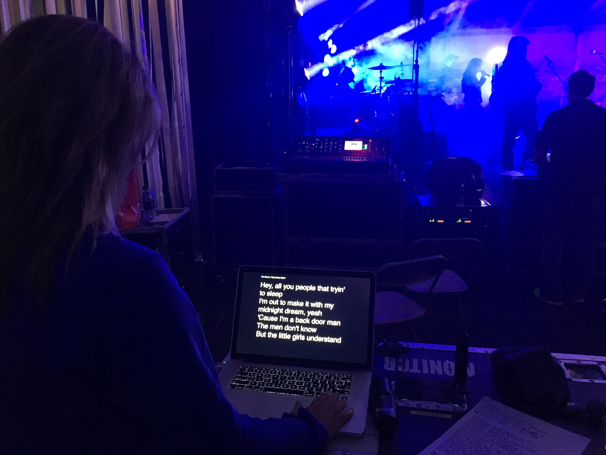 Operator running lyric prompts on a laptop in front of a blue-lit live band performance