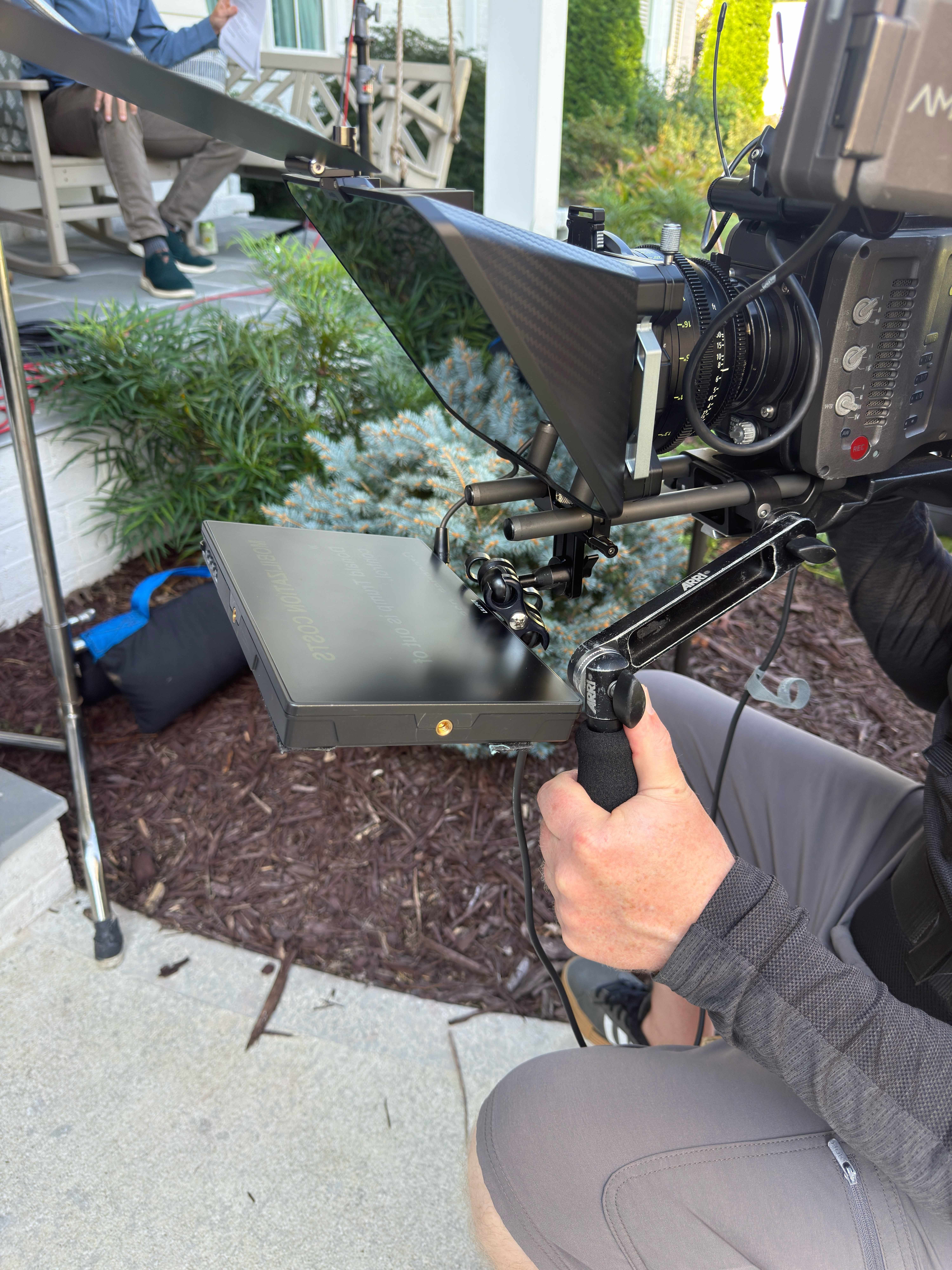 ARRI cinema camera with a carbon-fiber through-the-lens teleprompter and monitor, held by an operator on a residential porch shoot