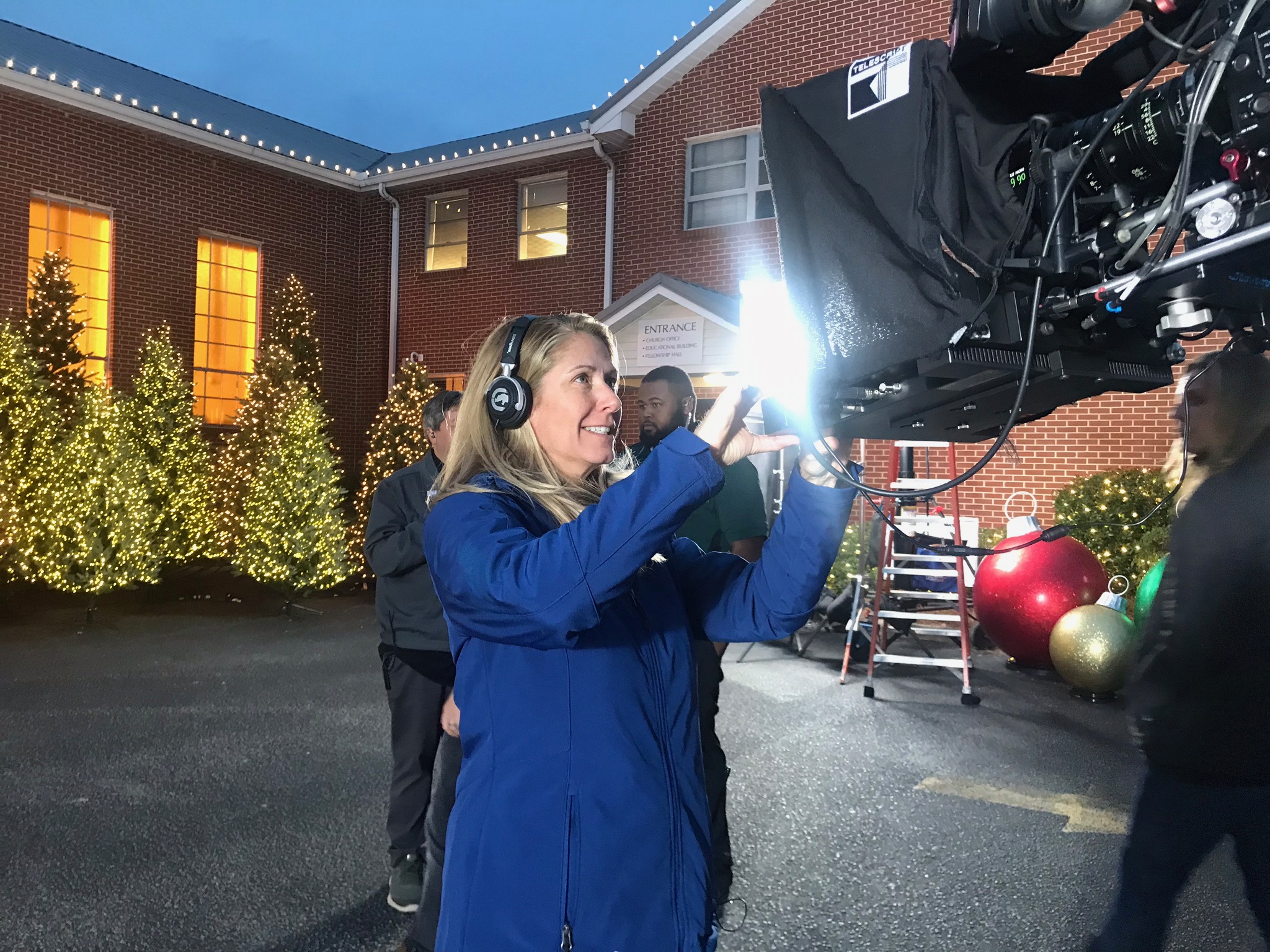 B Prompt operator in a headset adjusting a Telescript teleprompter at dusk by a holiday-lit venue